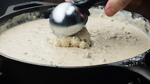 biscuit dough being dropped into sausage gravy
