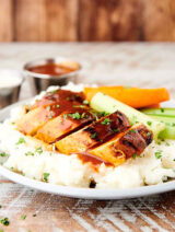 sliced buffalo chicken over mashed potatoes on plate with celery and carrots