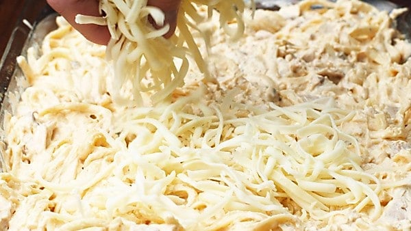 pasta in baking dish being sprinkled with cheese