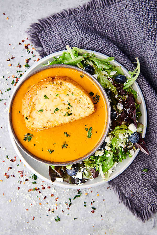 tomato basil soup in bowl on plate with salad above
