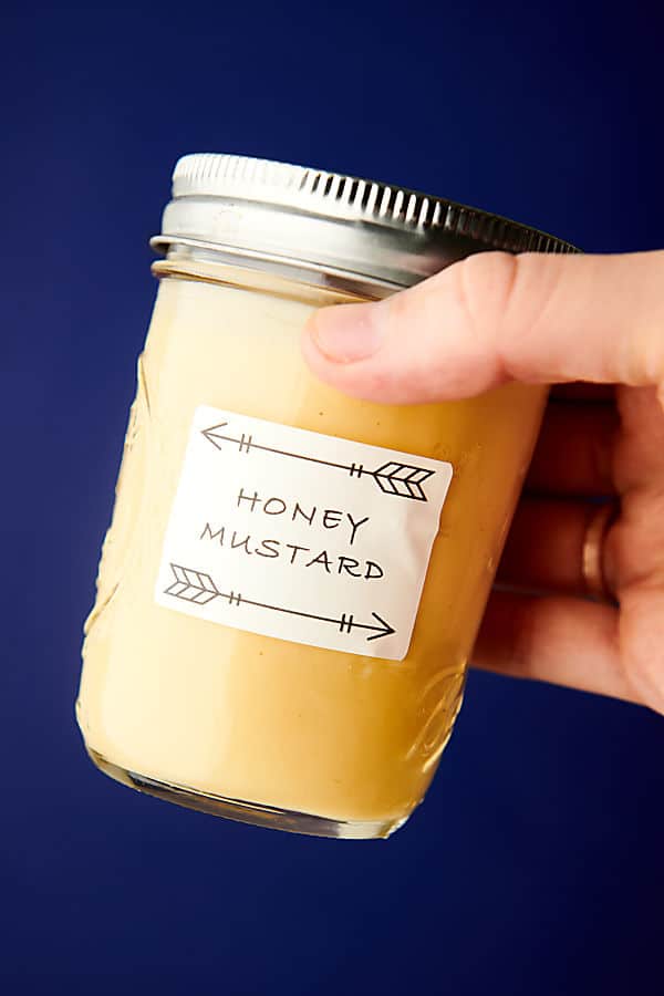 jar of honey mustard held blue background