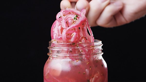 pickled red onions being taken out of jar with fork