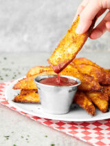 potato wedges on plate, one being dipped into ketchup