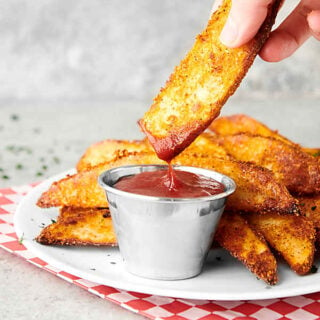 potato wedges on plate, one being dipped into ketchup