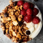almond butter granola in bowl with yogurt and raspberries above