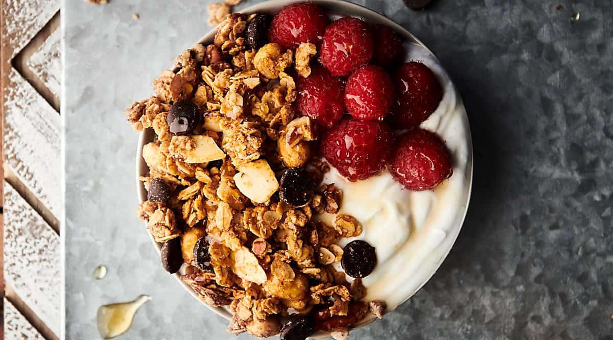 almond butter granola in bowl with yogurt and raspberries above