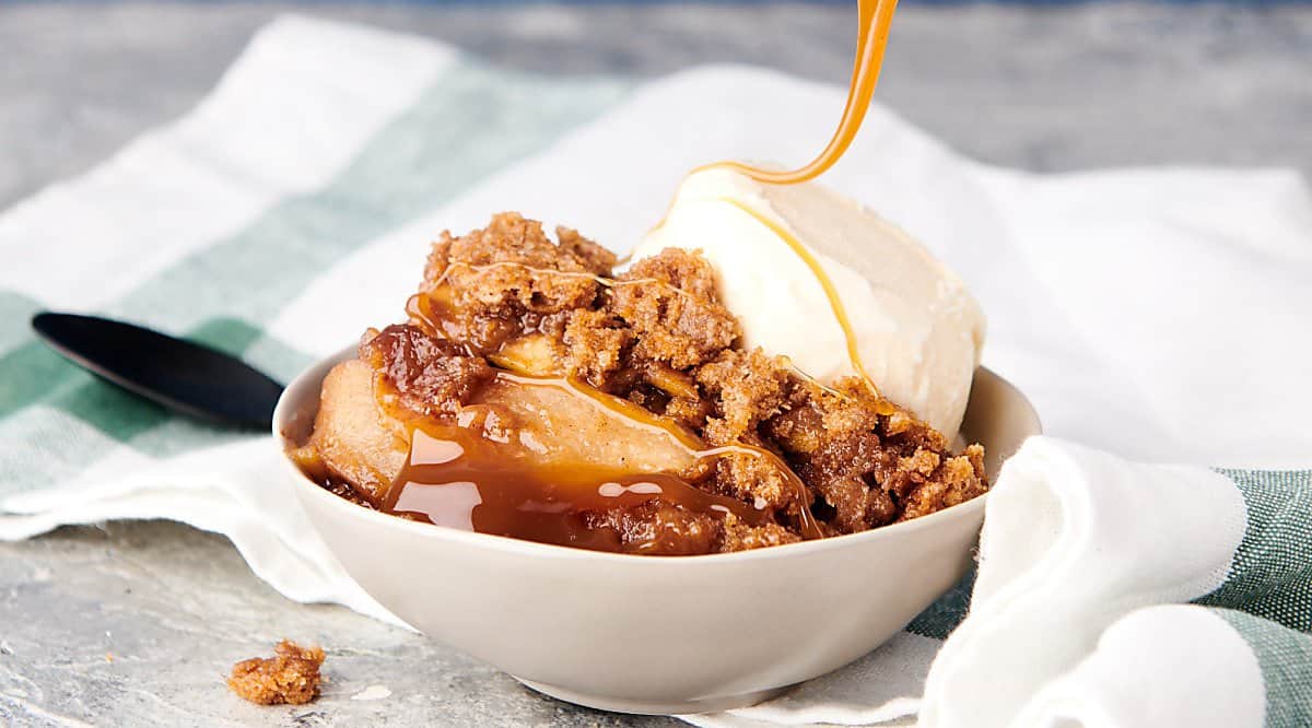 bowl of apple crumble being drizzled with caramel
