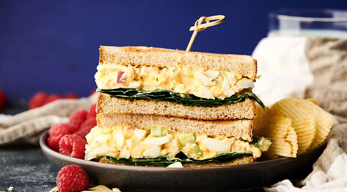 two halves of egg salad sandwich stacked on plate