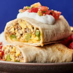 two halves of make ahead breakfast burritos stacked on plate with strawberries