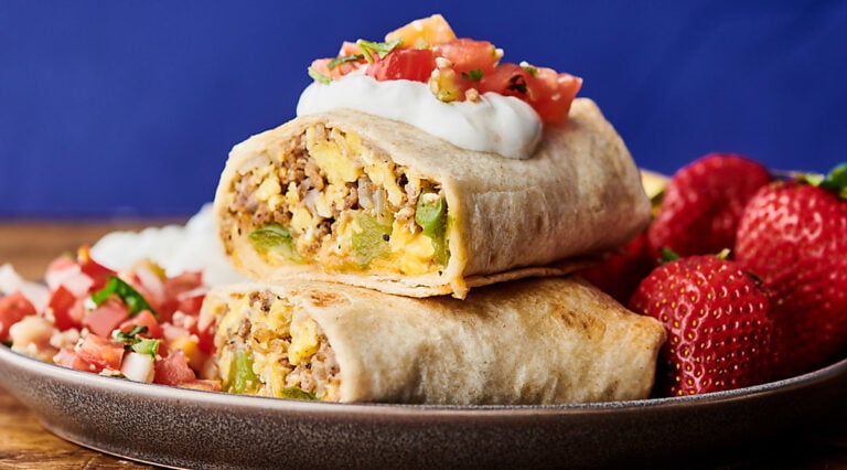 two halves of make ahead breakfast burritos stacked on plate with strawberries