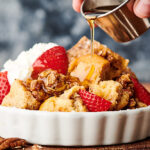 bowl of french toast casserole being drizzled with maple syrup