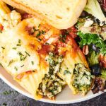 manicotti on plate with salad and garlic bread above