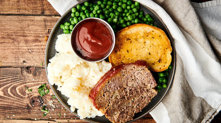 meatloaf on plate with bread, potatoes, and peas above