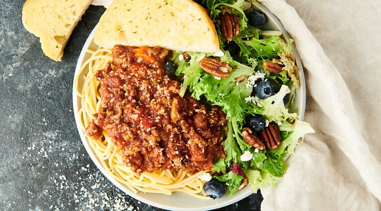 spaghetti bolognese on plate with salad and garlic bread above