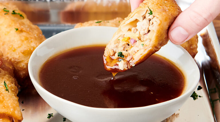 egg roll being dipped into bowl of sweet and sour sauce