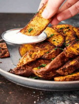air fryer potato wedges on plate, one being dipped in sauce