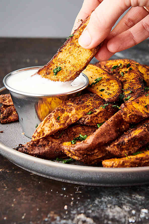 air fryer potato wedges on plate, one being dipped in sauce