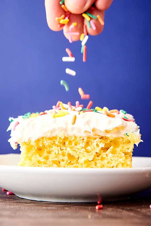 sprinkles being put on slice of cake on plate