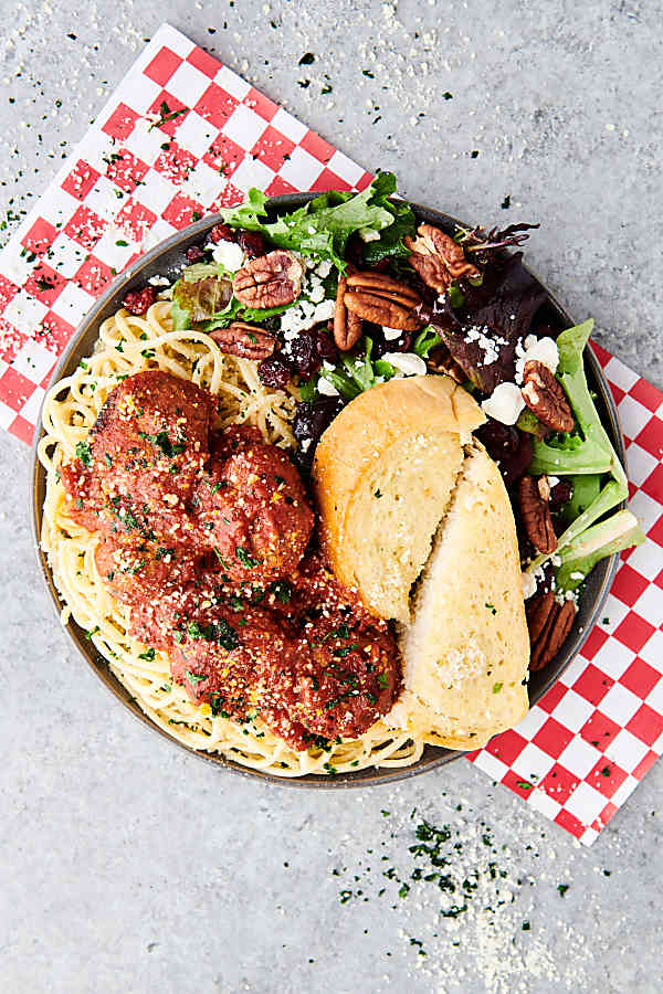plate of crockpot turkey meatballs over pasta with garlic bread and salad above