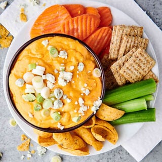 bowl of instant pot buffalo chicken dip on plate with carrots, crackers, celery, and chips above