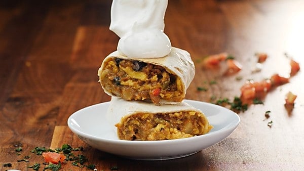 baked breakfast burrito on plate being topped with sour cream