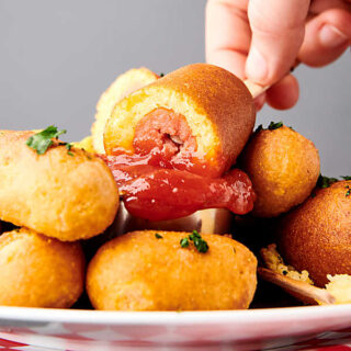 air fryer corn dogs on plate, one being dipped into ketchup