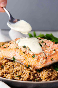 baked salmon over rice being drizzled with honey lemon sauce