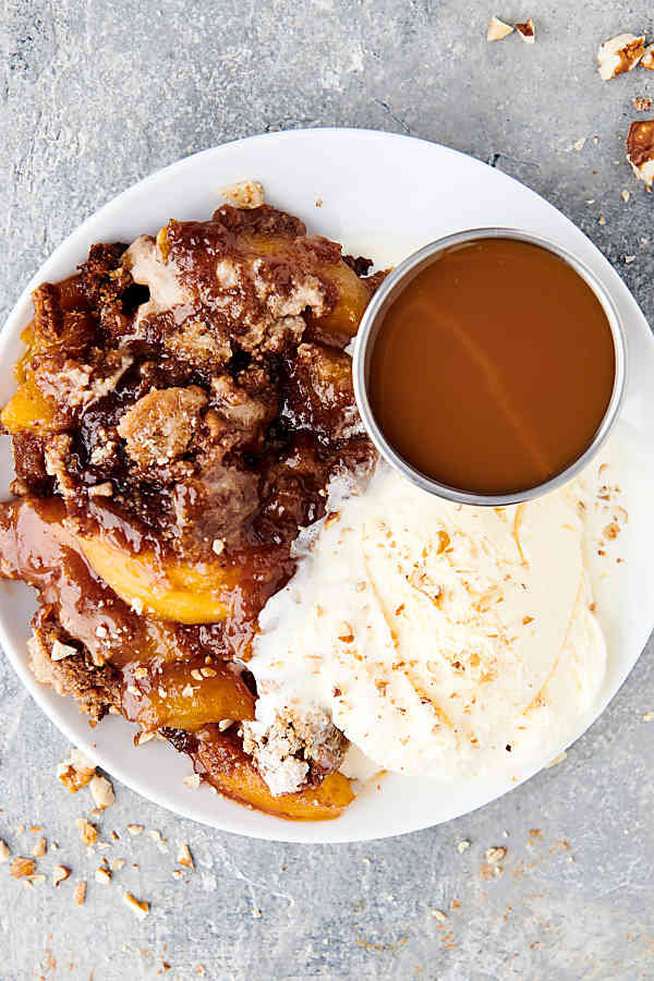 plate of peach cobbler next to vanilla ice cream and caramel above