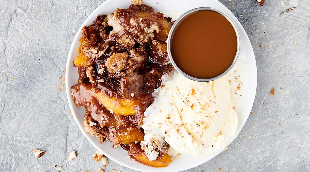 plate of crockpot peach cobbler with caramel and ice cream above