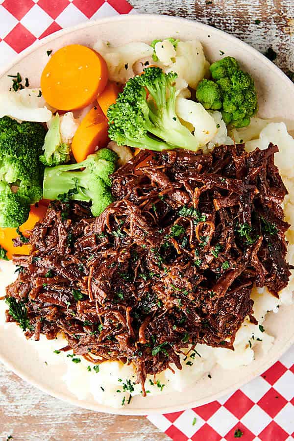 plate of slow cooker flank steak over mashed potatoes with veggies above