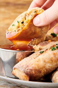 air fryer egg roll being dipped in sweet and sour sauce