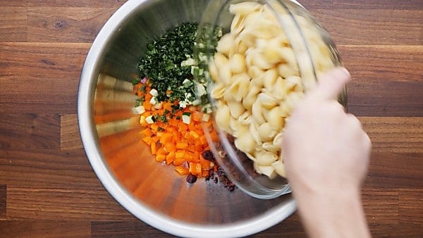 vegan pasta salad ingredients being placed into mixing bowl