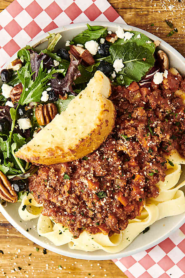 plate of bolognese with pasta, bread, and salad
