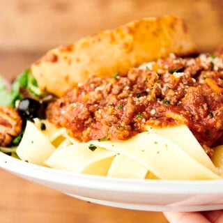 holding plate of bolognese on pasta