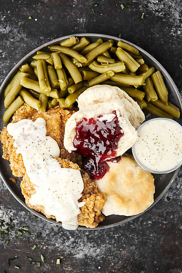 plate of food with fried chicken, country gravy, biscuits and jam, and green beans