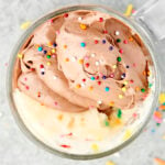 vanilla mug cake in a clear mug with chocolate frosting and sprinkles