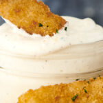 one fish stick dipping into a jar of lemon aioli