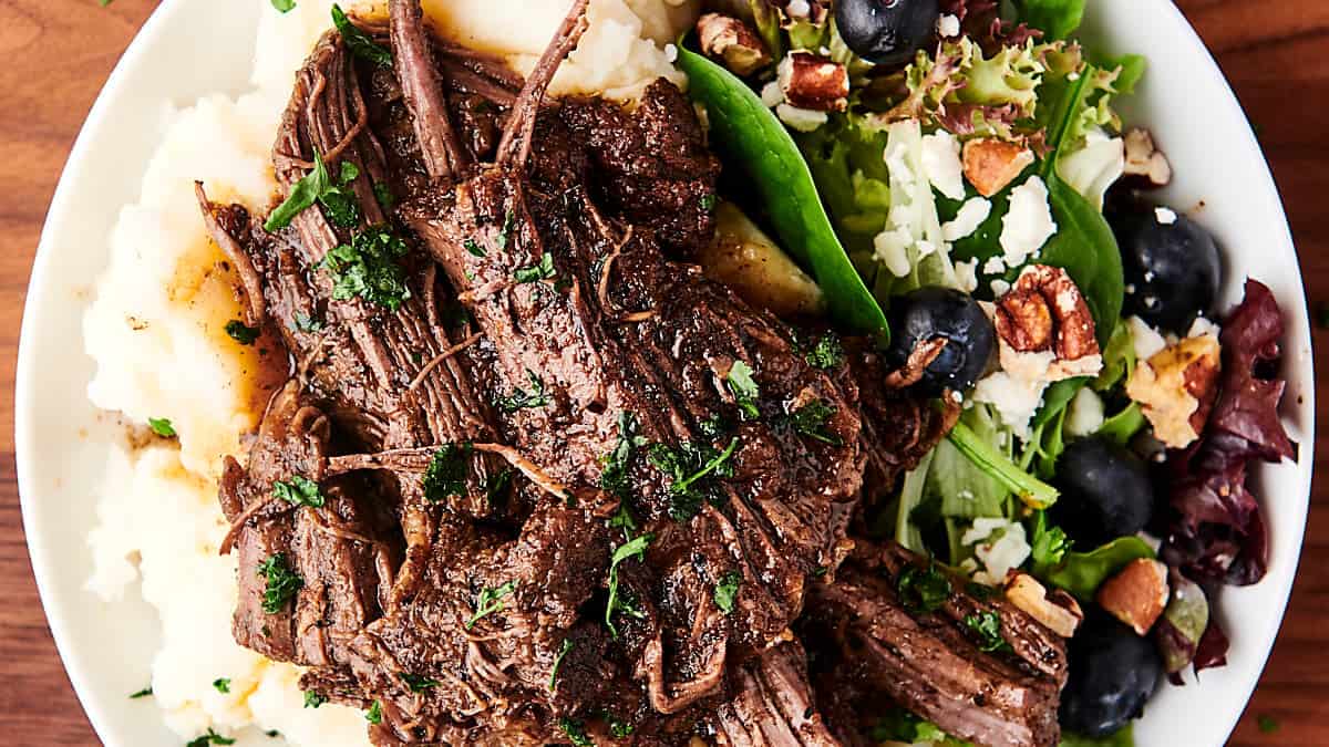 braised beef on a plate with potatoes and salad