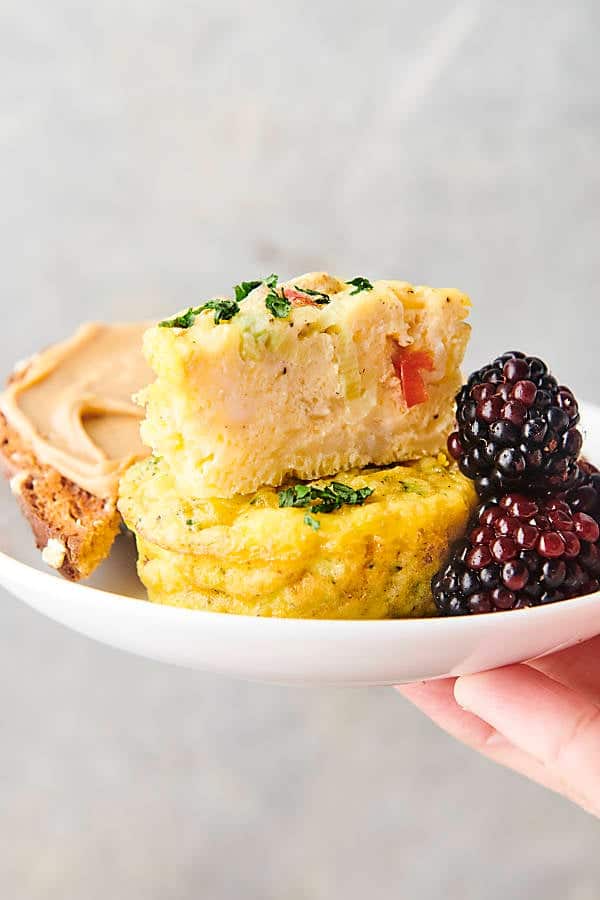holding a plate of protein egg muffins with toast and berries