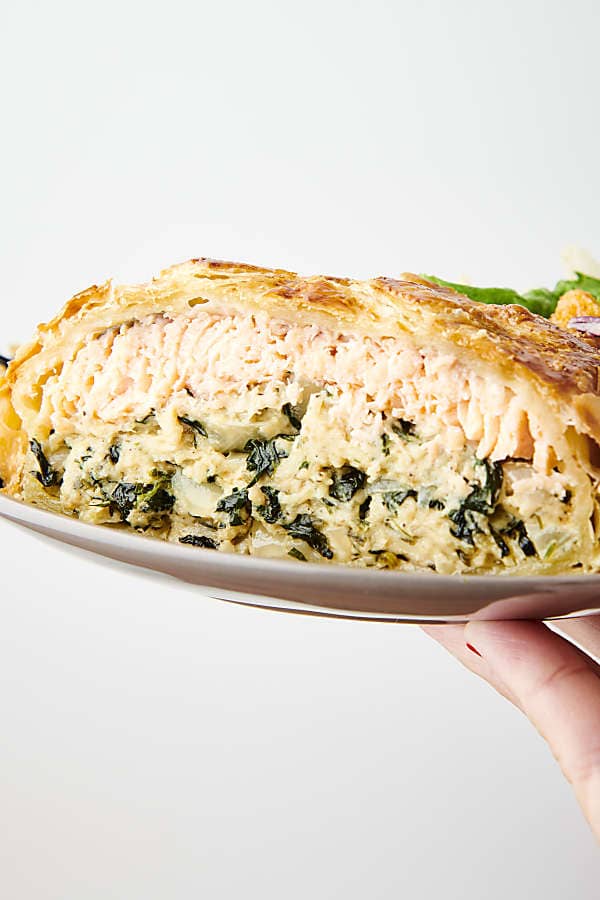 holding a plate with a slice of salmon wellington