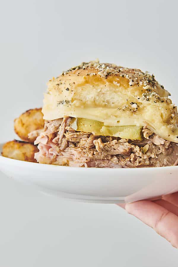 holding a plate with a cuban slider and tater tots