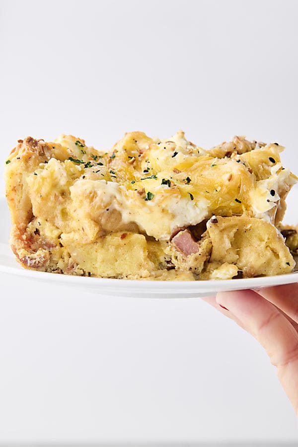 holding a plate with a slice of bacon egg and cheese bagel breakfast bake