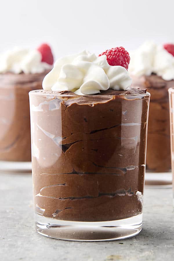 easy chocolate mousse in glasses topped with whipped cream and raspberries