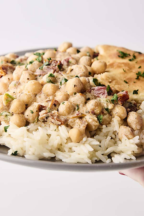 holding a plate of creamy sun dried tomato coconut milk chickpeas