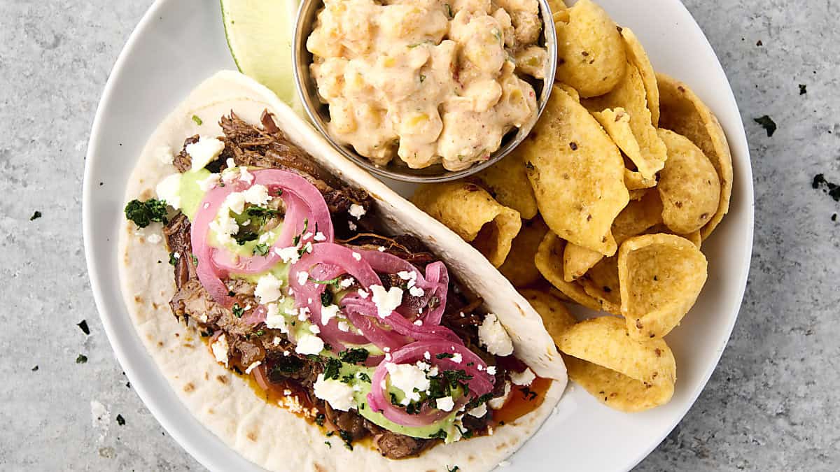 crockpot chuck roast tacos on a plate with corn dip and fritos