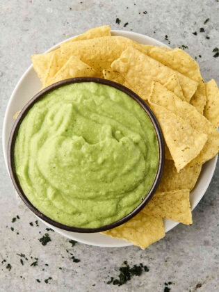 avocado dip in a bowl with chips on the side