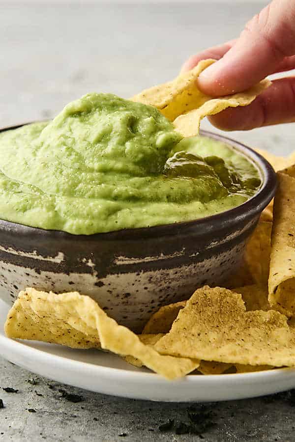 scooping avocado dip with a chip