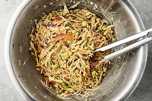 peanut noodle salad tossed together in a bowl with tongs