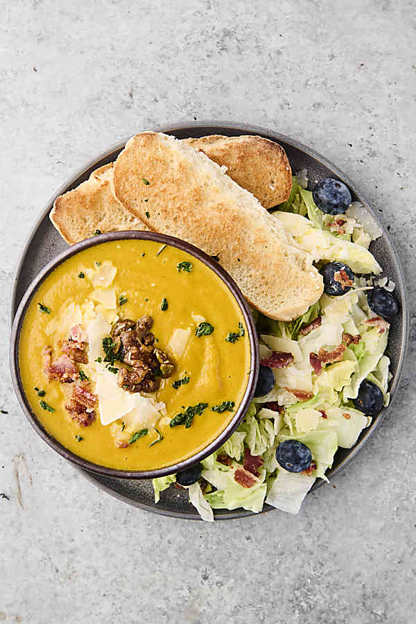 pumpkin soup in a bowl served with salad and bread