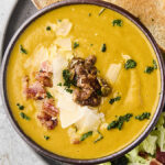 canned pumpkin soup recipe in a bowl with nuts, bacon, and cheese for toppings
